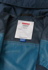 Giacca per bambini Reima con uno strato esterno blu navy, fodera in rete, etichetta con dettagli del marchio e della taglia, e etichetta bluesign®.