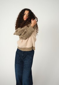Strickpullover mit einem Farbschema in Beige und Braun und strukturierten Ärmeln. Kombiniert mit dunkelblauen weiten Denim-Hosen.