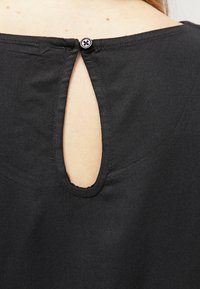 Czarna bluzka z tkaniny z okrągłym wycięciem na plecach, zapinana na czarny guzik. Gładka faktura i prosty design.