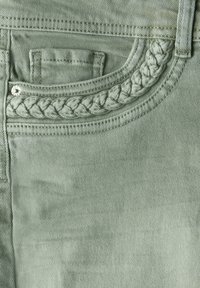 Helles grünes Denim-Gewebe mit einer geflochtenen Akzentuierung im Bereich der Tasche. Verfügt über kontrastierende Nähte und ein silbernes Metall-Druckknopfdetail.