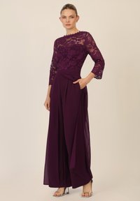 Top viola in pizzo con design floreale e maniche a tre quarti, abbinato a pantaloni larghi plissettati e fluidi, dotati di tasca laterale.