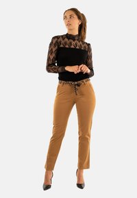 Zwarte kanten top met lange mouwen en hoge hals, gecombineerd met bruine slim-fit broek met een luipaardprint riem en zwarte hoge hakken.