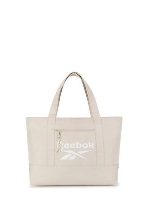 Beige Reebok Tragetasche mit zwei Schulterriemen, einer Reißverschlusstasche vorne und weißem Reebok-Logo samt Vektor-Design auf der Tasche.