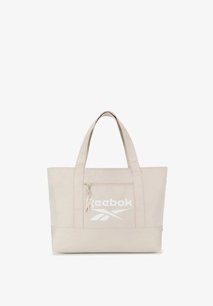Beżowa torba Reebok na ramię z dwoma paskami na ramię, przednią kieszenią na zamek oraz białym logo Reebok i wzorem wektorowym na kieszeni.