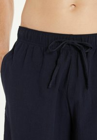 Námořnické modré lněné kalhoty s elastickým pasem, stahovací šňůrkou a dvěma bočními kapsami, s uvolněným střihem a hladkým povrchem.