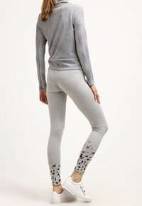 Šedé tričko s dlouhým rukávem a texturovaným vzorem, doplněné šedými legínami s černými abstraktními vzory na lemu. Kombinováno s bílými teniskami.