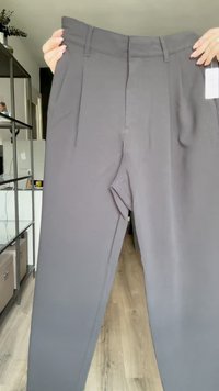 Calças cinzas com um design de perna reta, apresentando pregas frontais, passadores de cinto e uma cintura lisa. Feitas de um tecido suave.