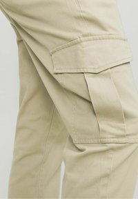 Beige cargo kalhoty se bočními kapsami, vyrobené z odolné bavlněné tkaniny. Obsahují dvojitě šité švy a rovný střih nohavic.
