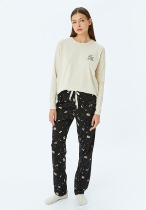 Beige lange mouwen top met de tekst "Magic"; zwarte broek met een speels patroon van muzieknoten en voorwerpen, voorzien van een trekkoord in de taille.