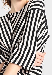 Mustavalkoinen raidallinen paita, jossa on rento istuvuus, pyöreä kaula-aukko ja leveät hihat. Sileä rakenne, jossa on vaakasuuntainen raitakuosi.