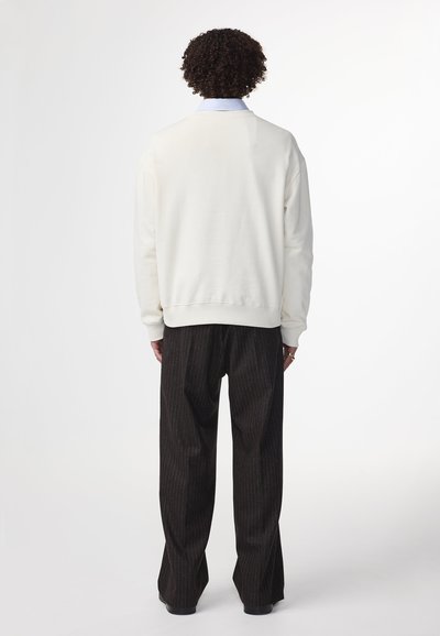 Hellfarbener Pullover mit Rundhalsausschnitt, gerippten Bündchen und unterem Saum; kombiniert mit dunklen Streifenhosen.