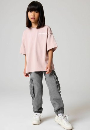 Lyselyserød oversized t-shirt med "ALLSAINTS" tekst, parret med grå cargo bukser med sidelommer og elastiske manchetter, afsluttet med hvide sneakers.