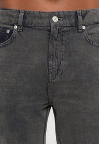 Črne jeans hlače iz denima z zbledelim videzom, s srebrnimi dodatki, petimi žepi ter zadrgo in gumbom za zapiranje.