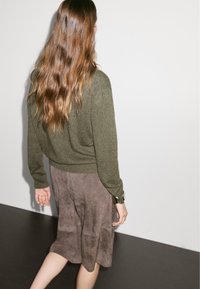 Maglione verde a maglia abbinato a una gonna in suede marrone. Il maglione ha i polsini aderenti e la gonna presenta un design fluido con pieghe.