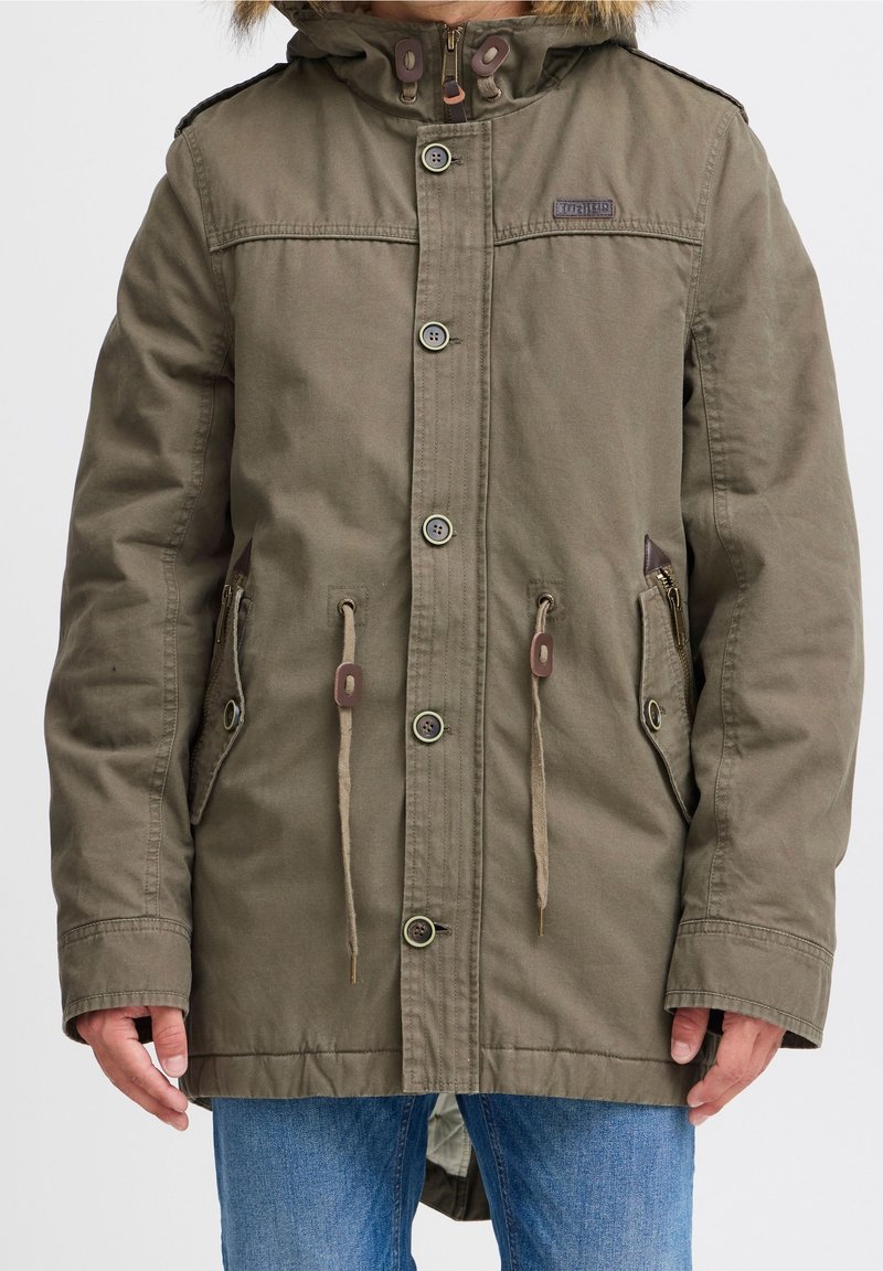 Olijfgroene parka met een capuchon gevoerd met bont, knoopsluitingen, trekkoorden in de taille en twee zijzakken.