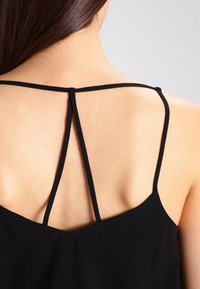 Top nero senza maniche con sottili spalline a spaghetto. Presenta un design minimalista nella parte posteriore con spalline incrociate e una texture liscia e morbida.