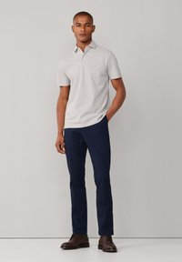 Polo de color gris claro con cuello, combinado con pantalones azul marino y zapatos de cuero marrón. El conjunto es sencillo y de diseño limpio.