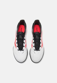 Zapatillas deportivas blancas con cordones y acentos negros, con detalles rojos en los laterales, textura suave y un diseño aerodinámico.