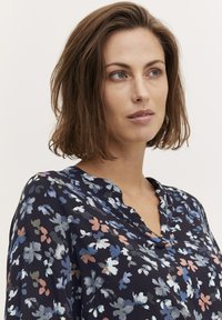 Blusa floreale in navy scuro con una consistenza morbida, caratterizzata da una scollatura a V e un motivo di fiori blu chiaro, rosa e verde sparsi.