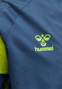 Blå sportstyg med en texturerad mönstring, med ljusgröna accenter och "hummel"-logotypen i ett stiliserat typsnitt.