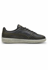 Must musta sneaker, mille kollane õmblus, ümar varvas, lame selge täpiline tall ja reljeefne logo keele peal. Klassikaline madala tipuga disain.