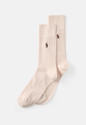 Calcetines acanalados beige hechos de algodón suave, con un pequeño logo marrón en los laterales. Tienen una textura suave y un diseño clásico.