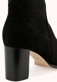 Bottine en suède noir avec un talon carré. Présente une texture lisse et une forme effilée, avec des détails de couture sur le côté.