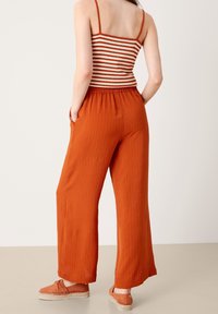 Oranžové kalhoty s širokými nohavicemi vyrobené z lehkého materiálu, s elastickým pasem. V kombinaci s pruhovaným topem na ramínka a espadrilkami.