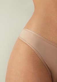Jasno beżowa bielizna o gładkiej fakturze, cienkiej talii i minimalnym pokryciu. Posiada bezszwowy design oraz miękki materiał dla komfortu.