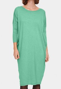 Grön, knälång klänning gjord av mjukt, texturerat tyg med lös passform, bred halsringning och trekvartslånga ärmar. Minimal design.