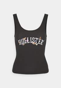 Svart ribbad linne med rundad halsringning, som har texten "HOLLISTER" i vitt, prydd med färgglada fjärils-illustrationer.