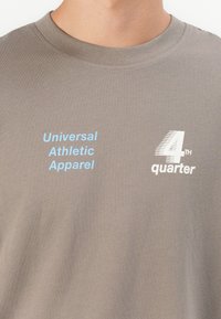 Grå bomulds t-shirt med rund hals. Har blå "Universal Athletic Apparel" og hvid "4th quarter" tekst i forskellige skrifttyper. Blød tekstur.