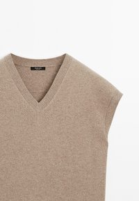 Beige pletená bezrukávová svetr vestička s výstřihem do V a žebrovanými okraji na rukávech a výstřihu, rozložená na bílém pozadí.