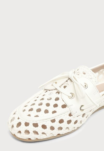 Mocassin en cuir tissé blanc avec motif en treillis ouvert, lacets à l'avant et semelle en cuir sur fond neutre.