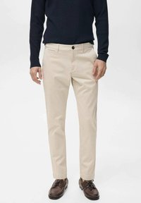 Beige chinos with a straight-leg design, featuring a single button closure and front pockets. Worn with a dark sweater and brown shoes.