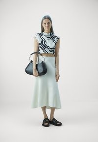 Black and white patterned crop top, white flared skirt, black handbag with a silver handle, and black slide sandals. Smooth textures throughout.