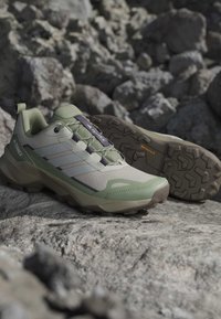 Chaussures de randonnée vert clair et beige avec semelles texturées reposant sur un terrain rocheux.