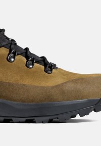 Bruine suède wandelschoen met zwarte veters, metalen oogjes en een dikke zwarte rubberen zool, ontworpen voor gebruik buitenshuis.