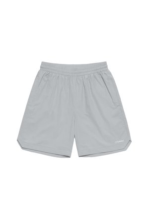 Mand iført lysegrå shorts, hvide mærkede sokker og sølvfarvede løbesko, stående med den ene hånd i lommen mod en ensfarvet baggrund.