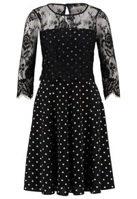 Svart klänning med spetsliv i blommönster, långa ärmar och kjol med prickar. Detalj med nyckelhål bak och utvikt form.