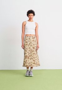 Beige en bruine rok met camouflagedessin tot de knie, met een rechte snit en twee zijzakken, gecombineerd met een witte crop top en sneakers.