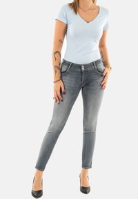 T-shirt bleu clair à col en V associé à un jean gris délavé slim. Le jean est doté d'une fermeture à bouton et de poches avant. Chaussures à talons hauts noires.