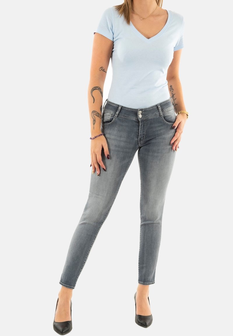 T-shirt bleu clair à col en V associé à un jean gris délavé slim. Le jean est doté d'une fermeture à bouton et de poches avant. Chaussures à talons hauts noires.