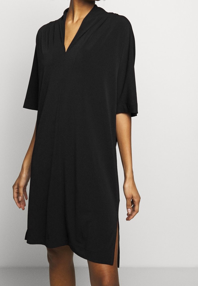 Robe noire à manches courtes avec un col en V, tissu doux, longueur genou, avec des fentes latérales et une coupe décontractée. Design simple et polyvalent.