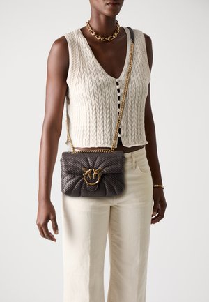 Gray woven handbag featuring a twisted design, gold hardware ring, and a shoulder chain strap, paired with a textured light-colored top.