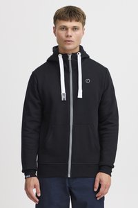Sudadera con cremallera negra y cordones blancos, cuenta con un bolsillo frontal, cremallera gris y un pequeño logo en el pecho. Textura suave y ajuste casual.
