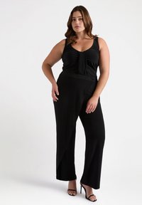 Zwarte jumpsuit met een aansluitende bovenkant, knoopdetail aan de voorkant en wijd uitlopende broekspijpen. Gemaakt van gladde stof, met een strakke, minimalistische uitstraling.