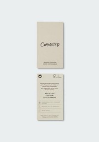 Etiqueta de cartulina con un fondo beige. Contiene la palabra "COMPROMETIDO" en texto negro en negrita. Enumera las características de sostenibilidad y los materiales ecológicos.