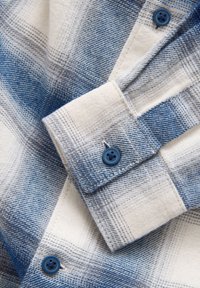 Close-up of cream and blue plaid flannel shirt sleeve and cuff with blue buttons.