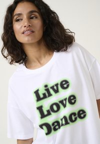 T-shirt en coton blanc avec un texte noir en gras disant "Vivez, Aimez, Dansez" avec un effet d'ombre vert vif. Manches courtes et coupe décontractée.